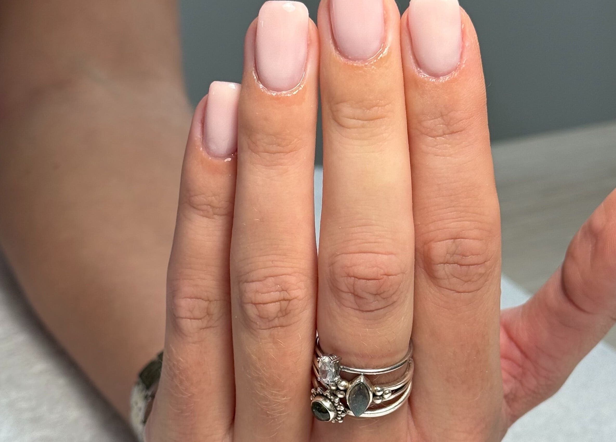 Elegant manicured nails at BAJE STUDIO, Burgess Hill, England, GB. Showcasing pink polish and silver rings.