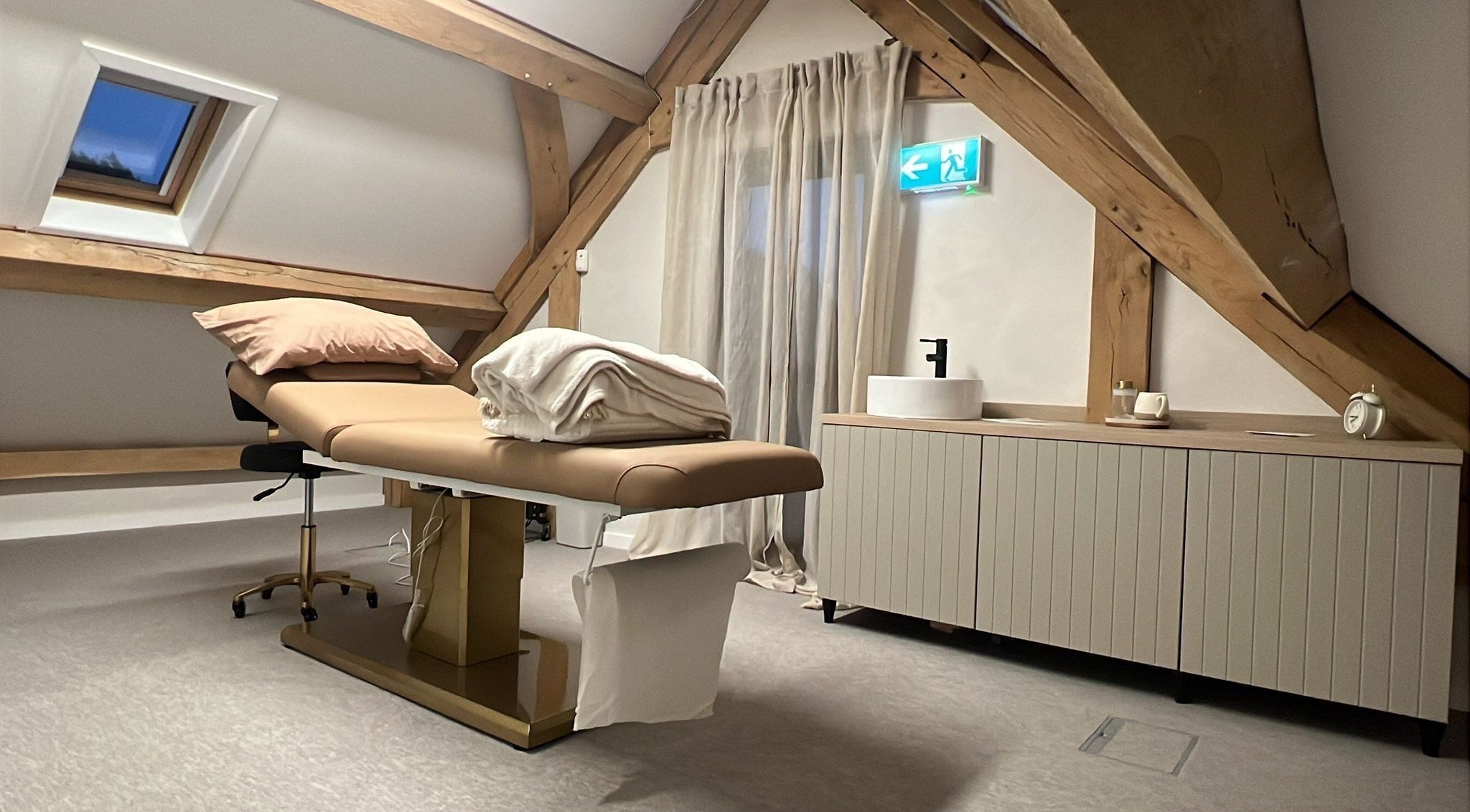Elegant treatment room at Tommo’s Treatments - Luxe Barn, Tickenham, England, GB with a massage table and wooden beams.