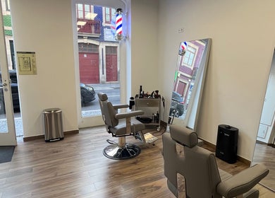 Interior moderno do UNIQ Barbershop em Póvoa De Varzim, Porto, PT, com cadeiras confortáveis e espelho grande.