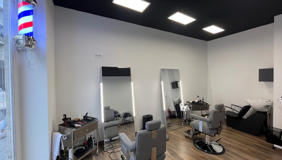 Interior moderno do UNIQ Barbershop em Póvoa De Varzim, Porto, PT com cadeiras de barbeiro e espelhos iluminados.