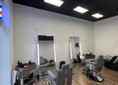 Interior moderno do UNIQ Barbershop em Póvoa De Varzim, Porto, PT com cadeiras de barbeiro e espelhos iluminados.
