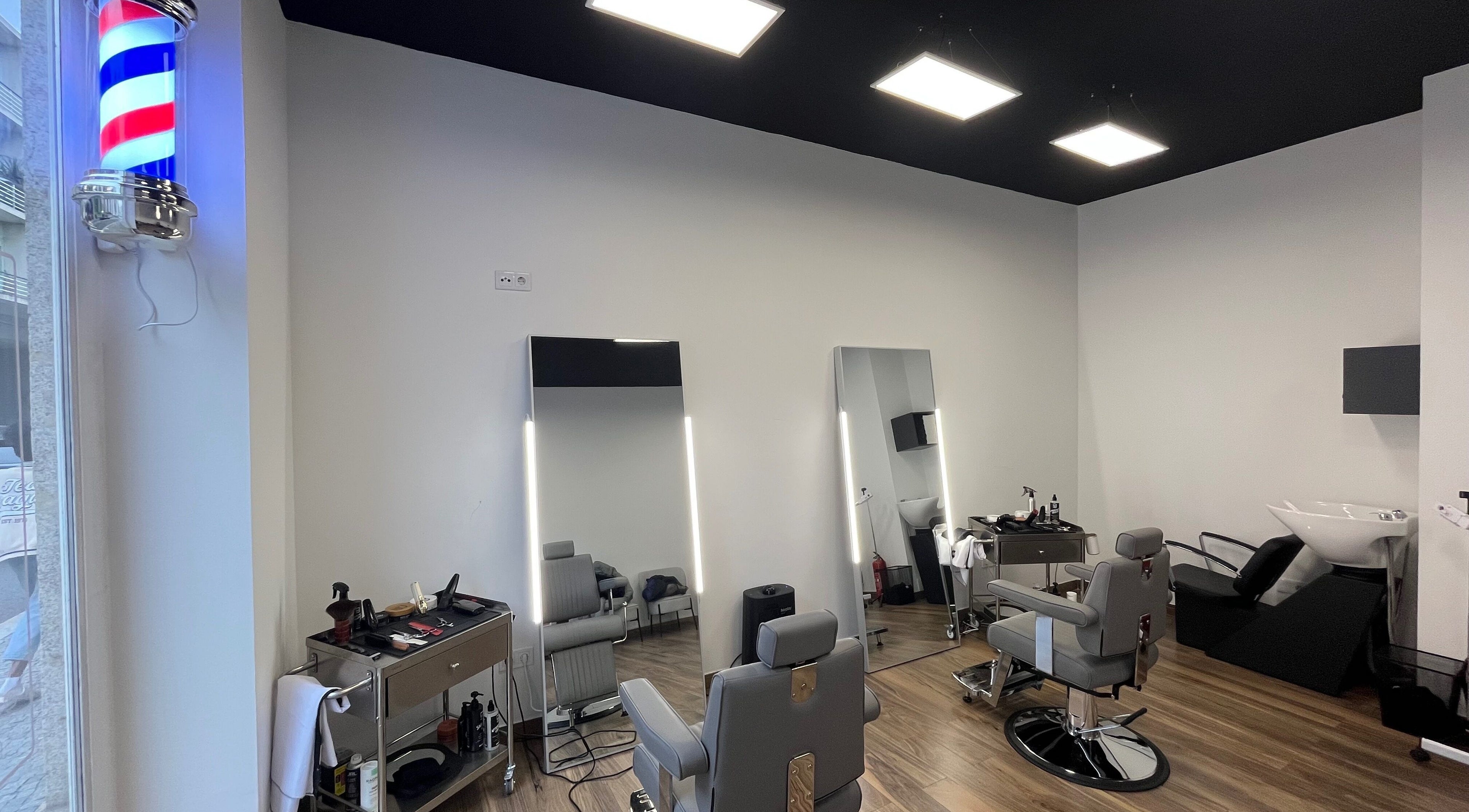 Interior moderno do UNIQ Barbershop em Póvoa De Varzim, Porto, PT com cadeiras de barbeiro e espelhos iluminados.