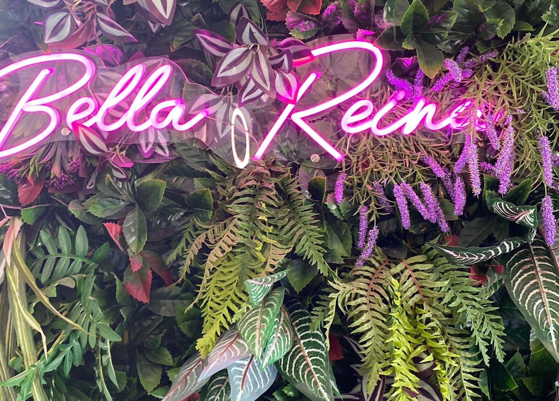 Neon Bella Reina aesthetics sign amidst lush greenery at Bridgwater, England, GB venue.