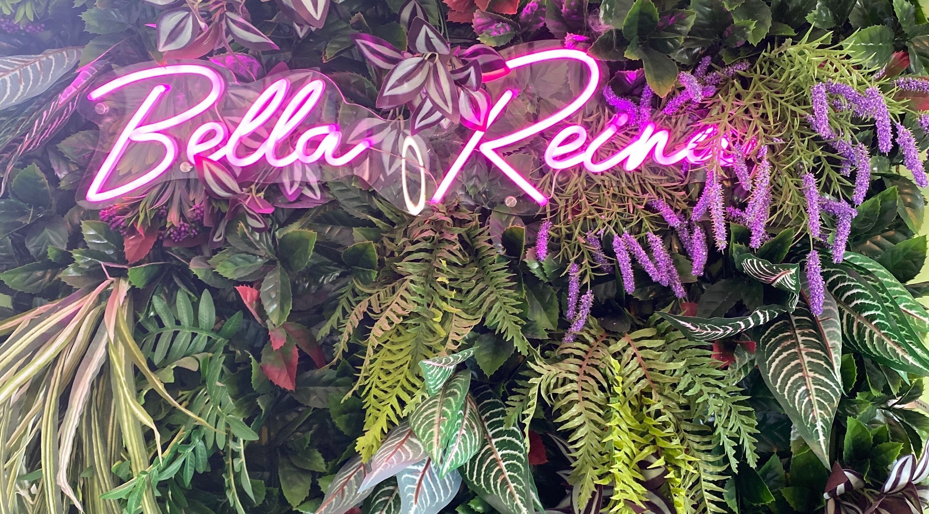Neon Bella Reina aesthetics sign amidst lush greenery at Bridgwater, England, GB venue.