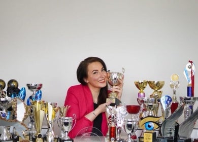 Person in pink blazer smiling with trophies at GlowHeadSpa, San Pawl Il-baħar, MT.
