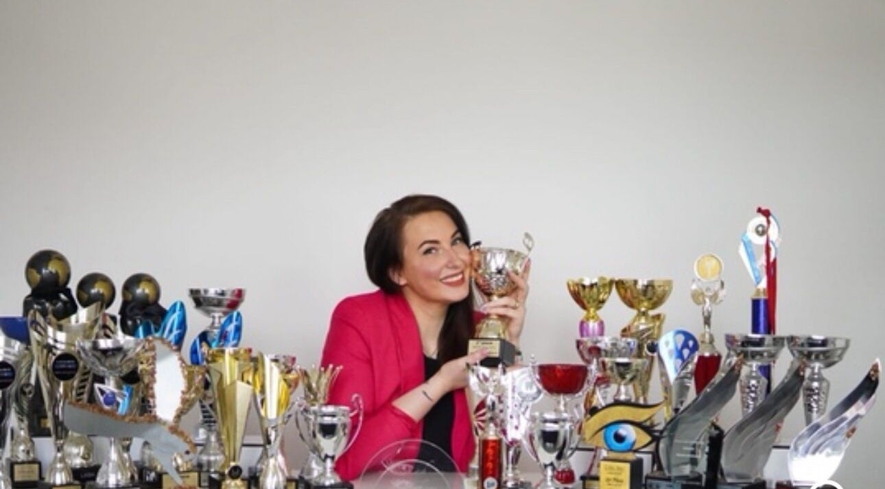 Person in pink blazer smiling with trophies at GlowHeadSpa, San Pawl Il-baħar, MT.