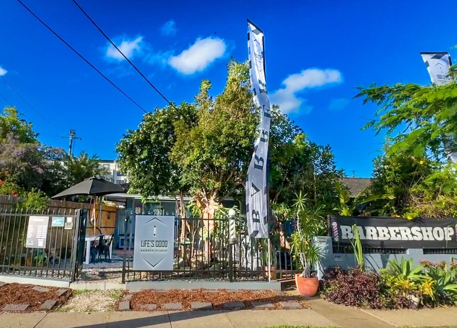 Lush entrance of Life’s Good Barber Studio in Cannon Hill, Queensland, AU, with vibrant greenery and banners.
