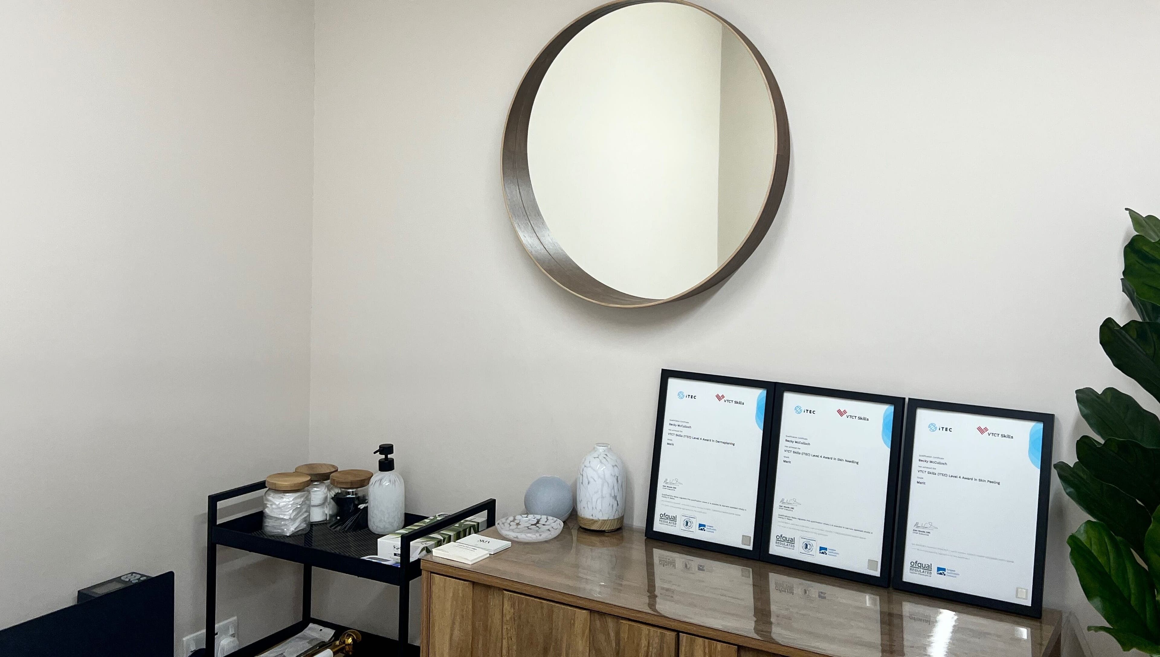 Elegant decor of Skin & Glo in Macclesfield, England, GB, featuring a round mirror and framed certificates.