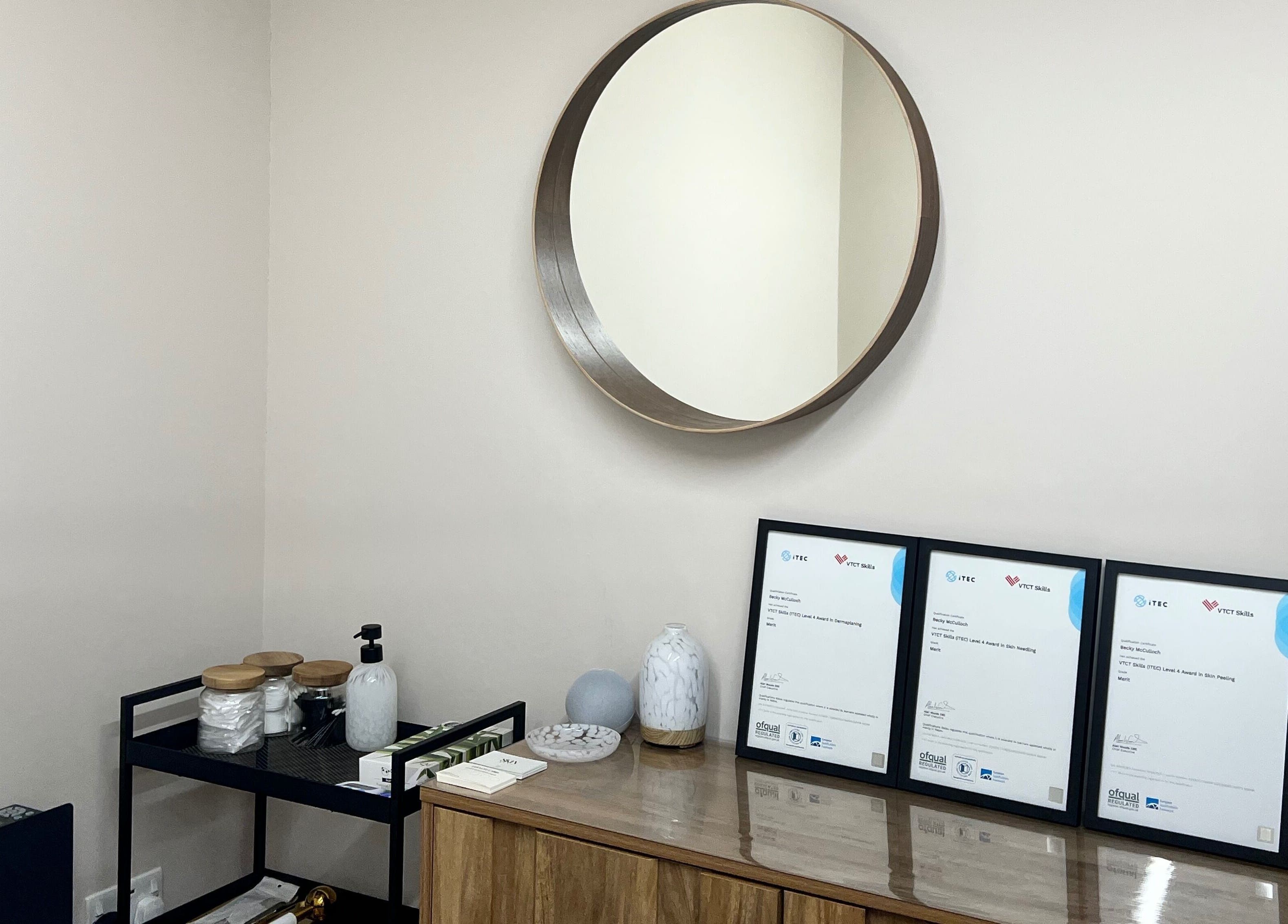Elegant decor of Skin & Glo in Macclesfield, England, GB, featuring a round mirror and framed certificates.