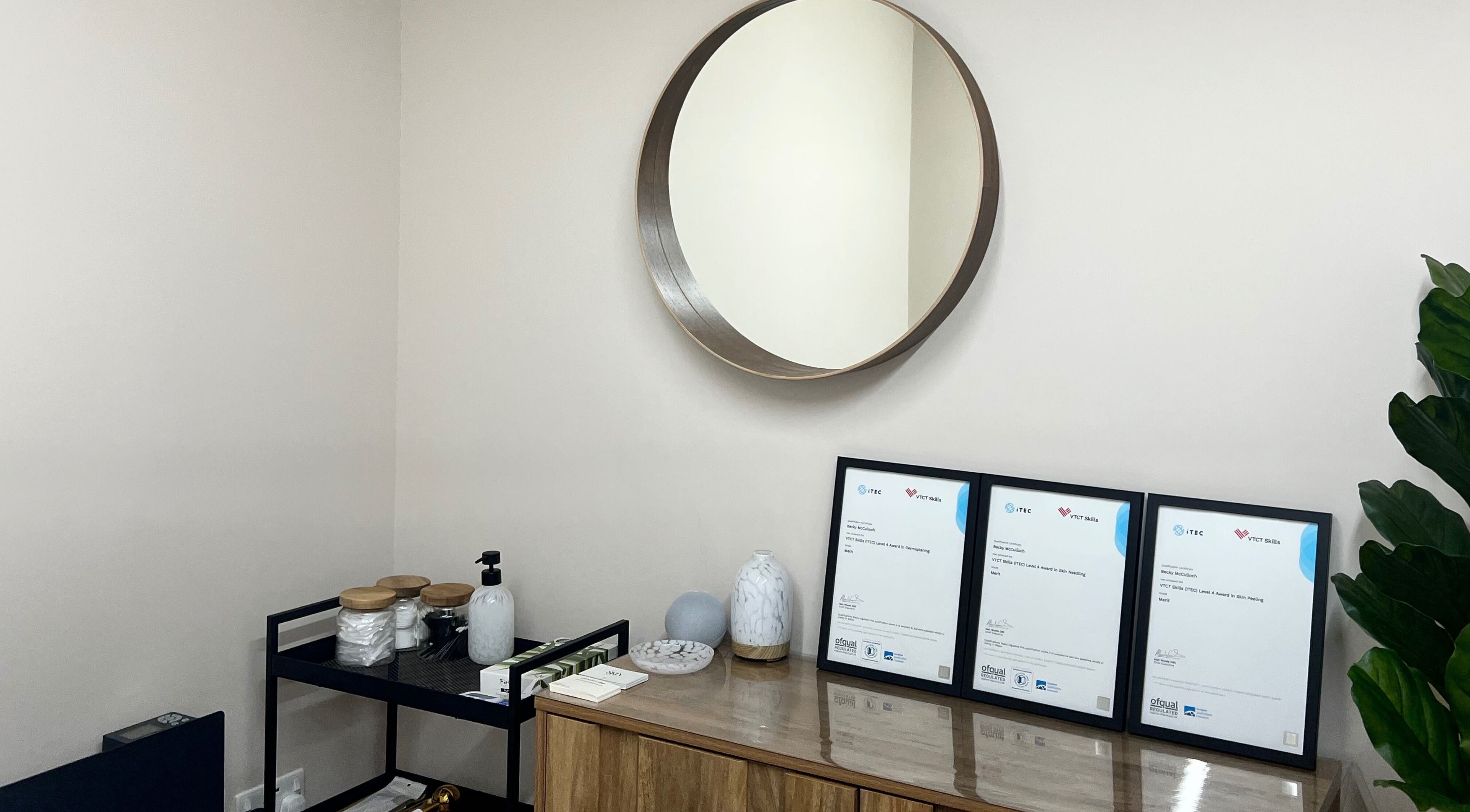 Elegant decor of Skin & Glo in Macclesfield, England, GB, featuring a round mirror and framed certificates.