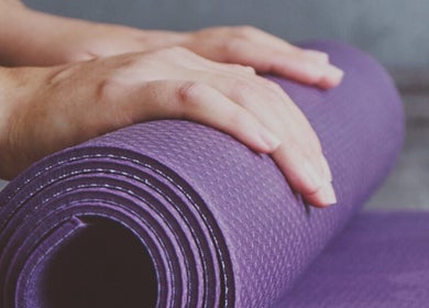 Hands prepare a purple yoga mat at FITLIVE, AE, setting a tranquil scene for wellness sessions.