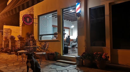 Η είσοδος του Xonikis Men’s Hair Studio στη Μεγάλη Παναγία, GR, φωτισμένη τη νύχτα με καλαίσθητες λεπτομέρειες.