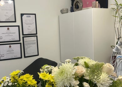 Interior of Naz Aesthetics in Manchester, England, GB, featuring framed certifications and elegant floral arrangements.