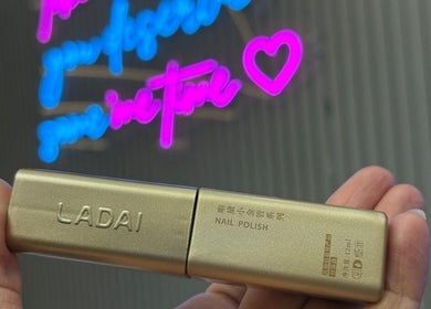 Gold nail polish held in Twinkle Toes, Parañaque, Metro Manila, PH beauty salon with neon sign in background.