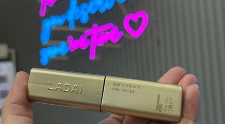 Gold nail polish held in Twinkle Toes, Parañaque, Metro Manila, PH beauty salon with neon sign in background.