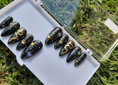 Elegant black and gold designer nails by Nails By Shaaquila, Roodepoort, Gauteng, ZA, on a grassy background.