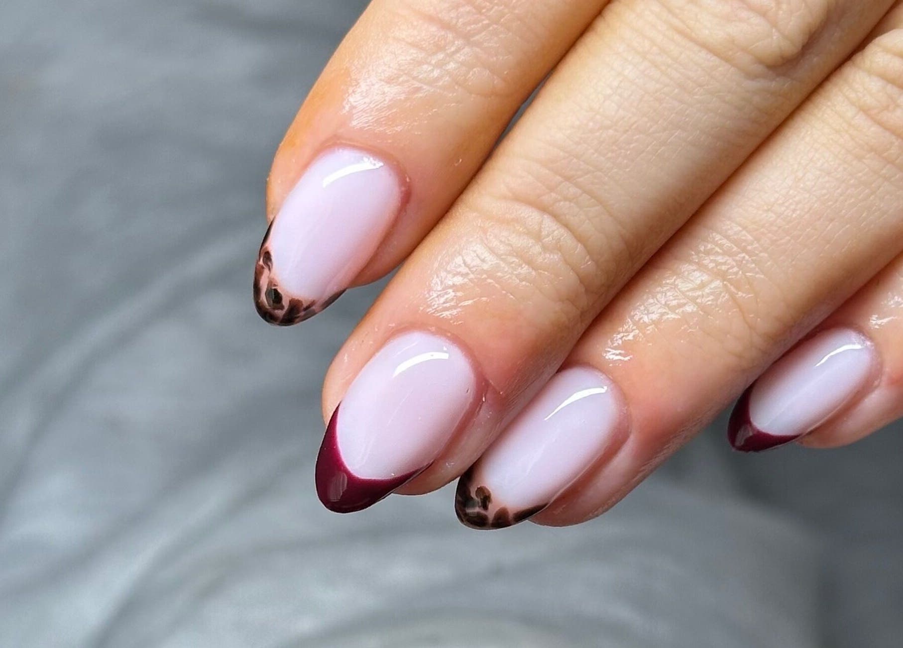 Stylish nail art at NAIAA Studio, Oakham, England, GB, featuring burgundy and leopard print tips.