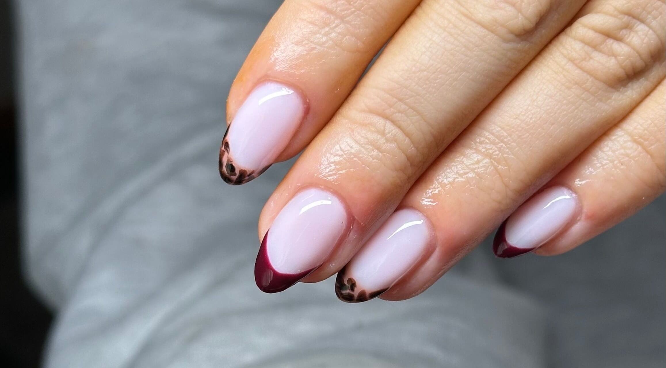 Stylish nail art at NAIAA Studio, Oakham, England, GB, featuring burgundy and leopard print tips.