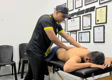 Skilled therapist performs massage at MAMU MASSAGE, Shah Alam, Selangor, MY. Walls adorned with certifications.