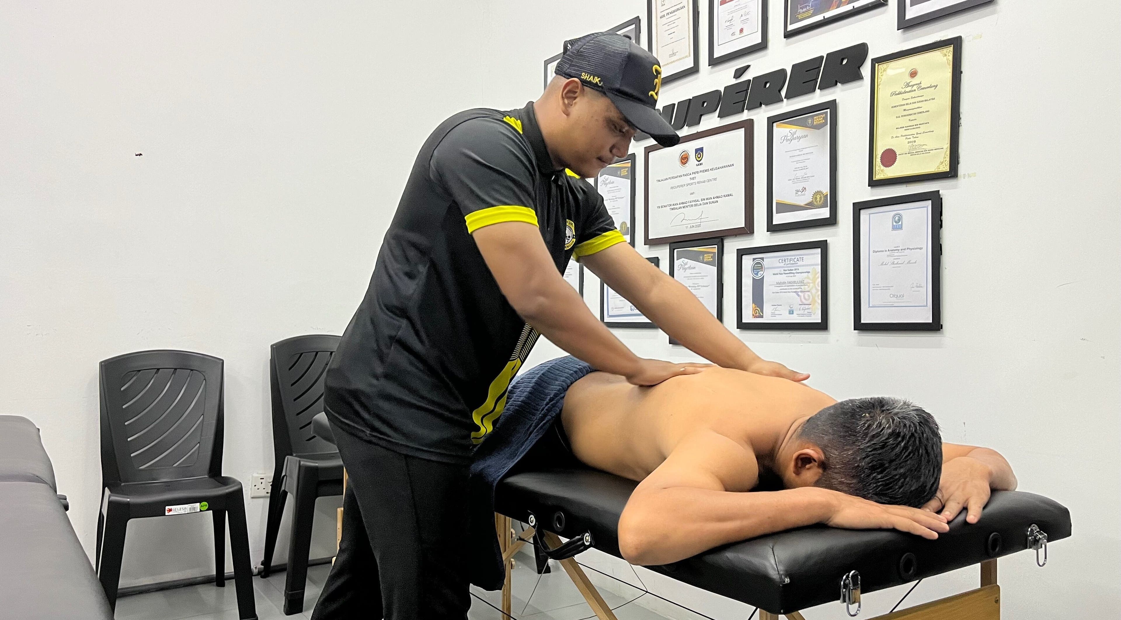 Skilled therapist performs massage at MAMU MASSAGE, Shah Alam, Selangor, MY. Walls adorned with certifications.