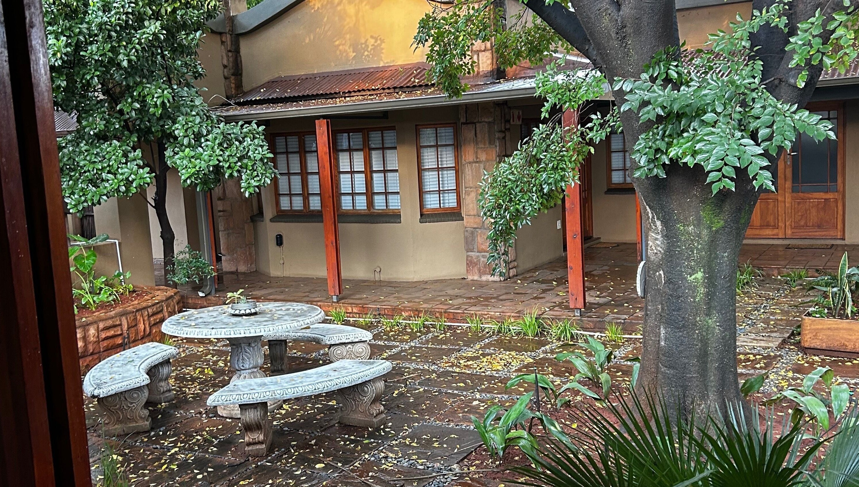 Serene courtyard at @PALACE in Potchefstroom, North West, ZA, featuring lush greenery and rustic seating.