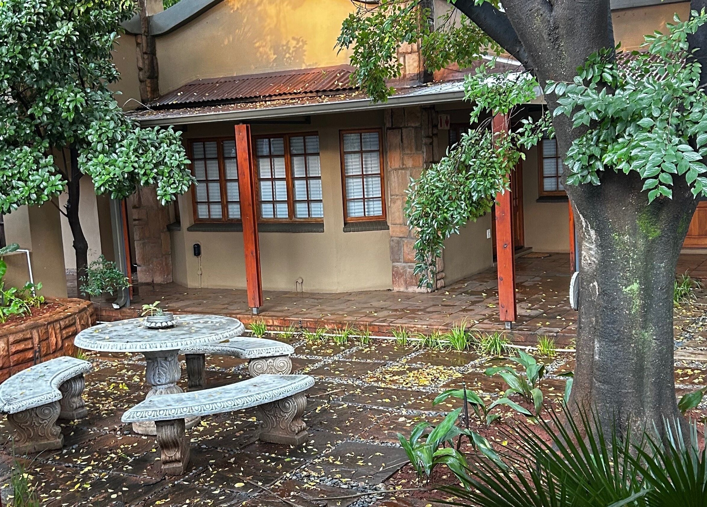 Serene courtyard at @PALACE in Potchefstroom, North West, ZA, featuring lush greenery and rustic seating.