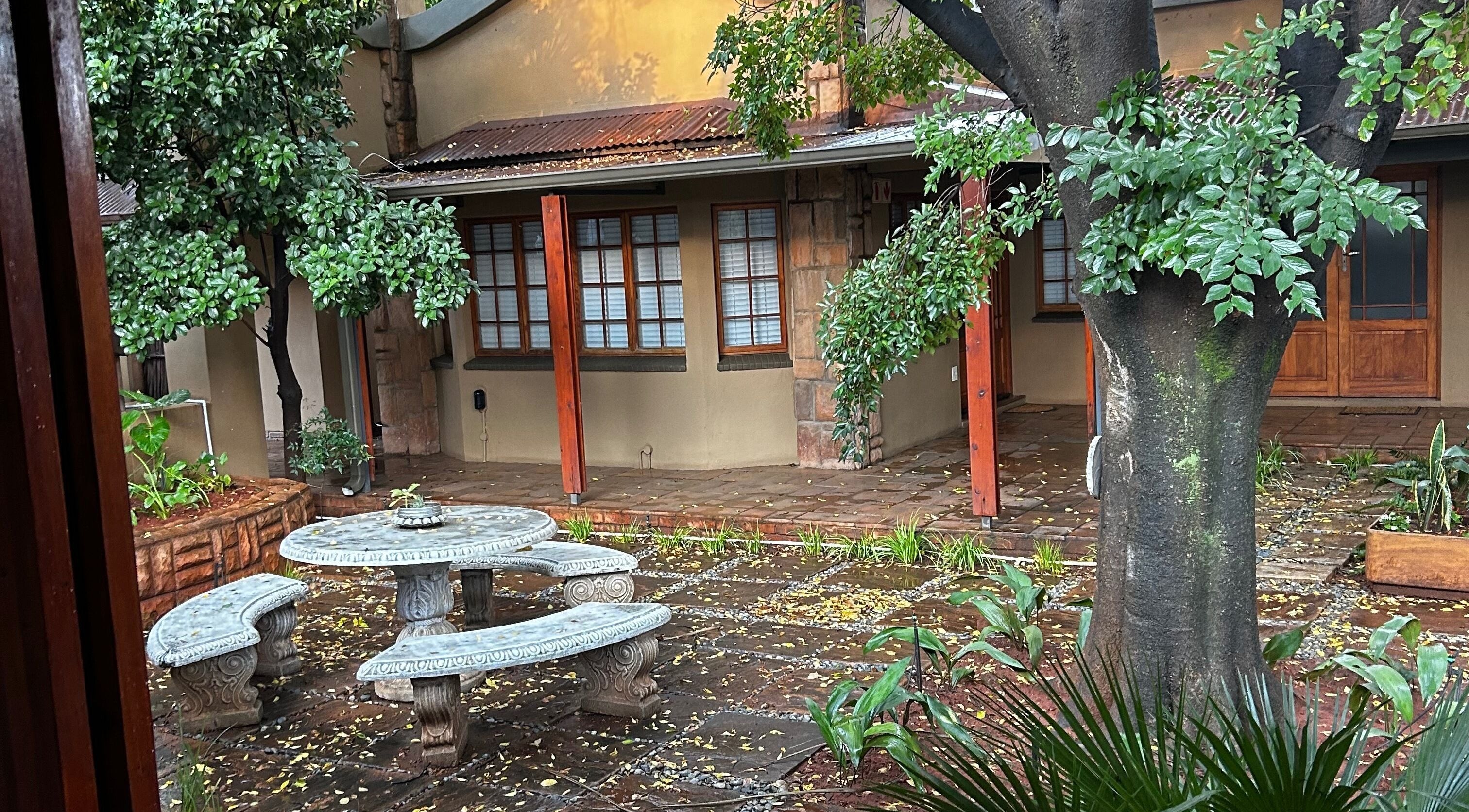 Serene courtyard at @PALACE in Potchefstroom, North West, ZA, featuring lush greenery and rustic seating.