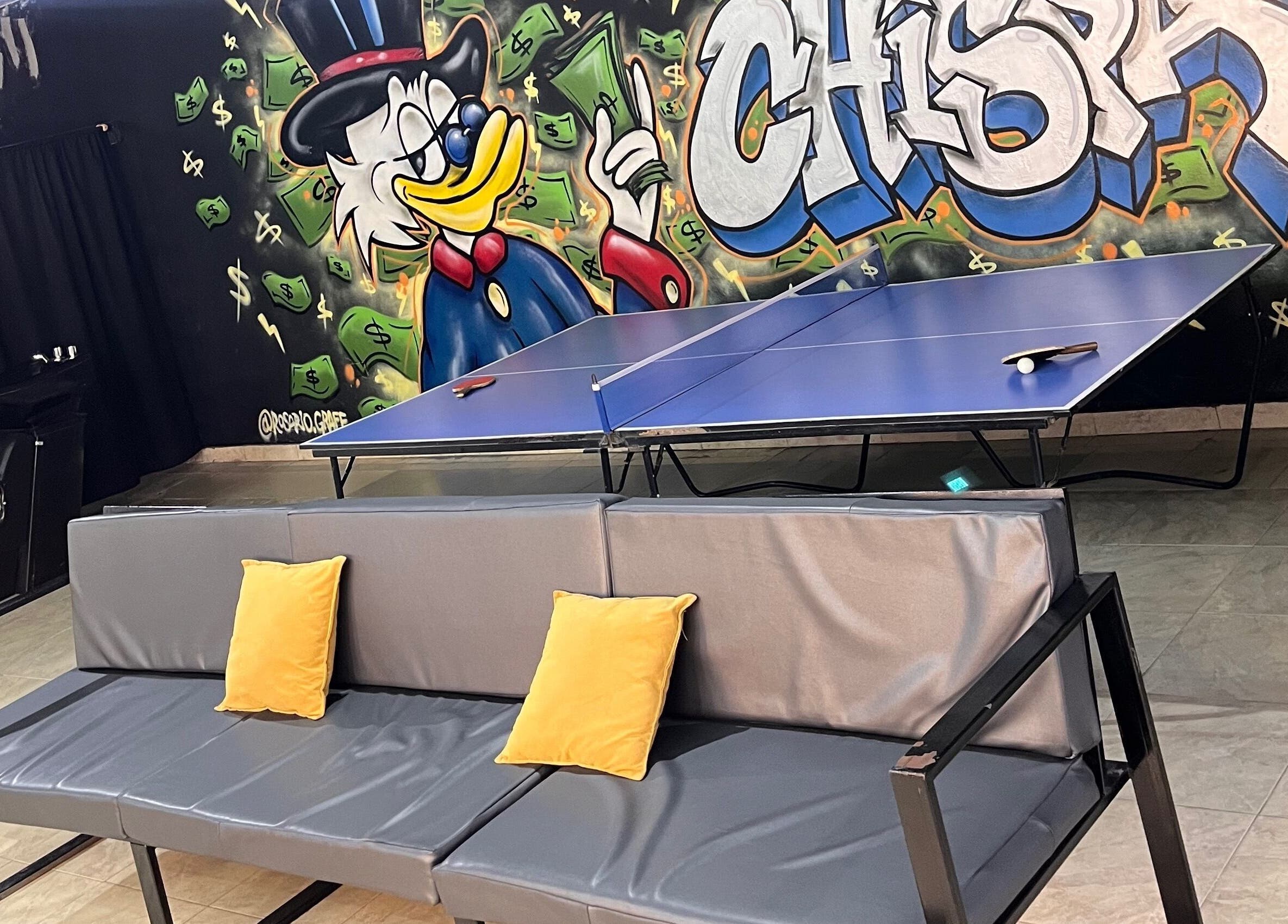 Colorful mural, couch, and ping pong table at Barbería La Chispa, Rosario, Santa Fe, AR inviting creative energy.