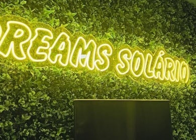 Neon 'Dreams Solário' sign at Lumera Nails, Figueira Da Foz, Coimbra, PT, on a lush green backdrop.
