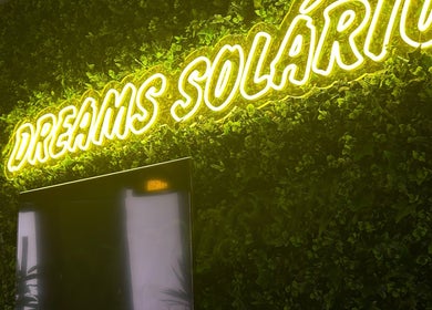 Vibrant neon 'Dreams Solário' sign at Lumera Nails, Figueira Da Foz, Coimbra, PT, surrounded by lush greenery.