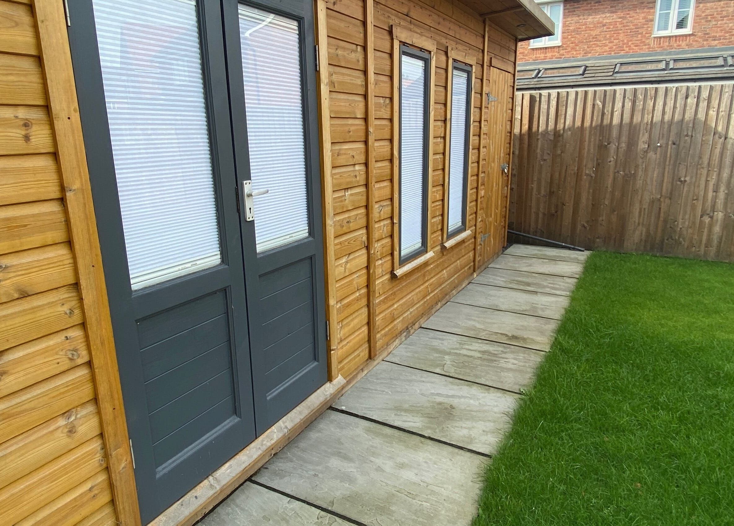 Charming exterior of House of Wax | Waxing Salon in St Helens, England, GB featuring wooden panels and lush greenery.