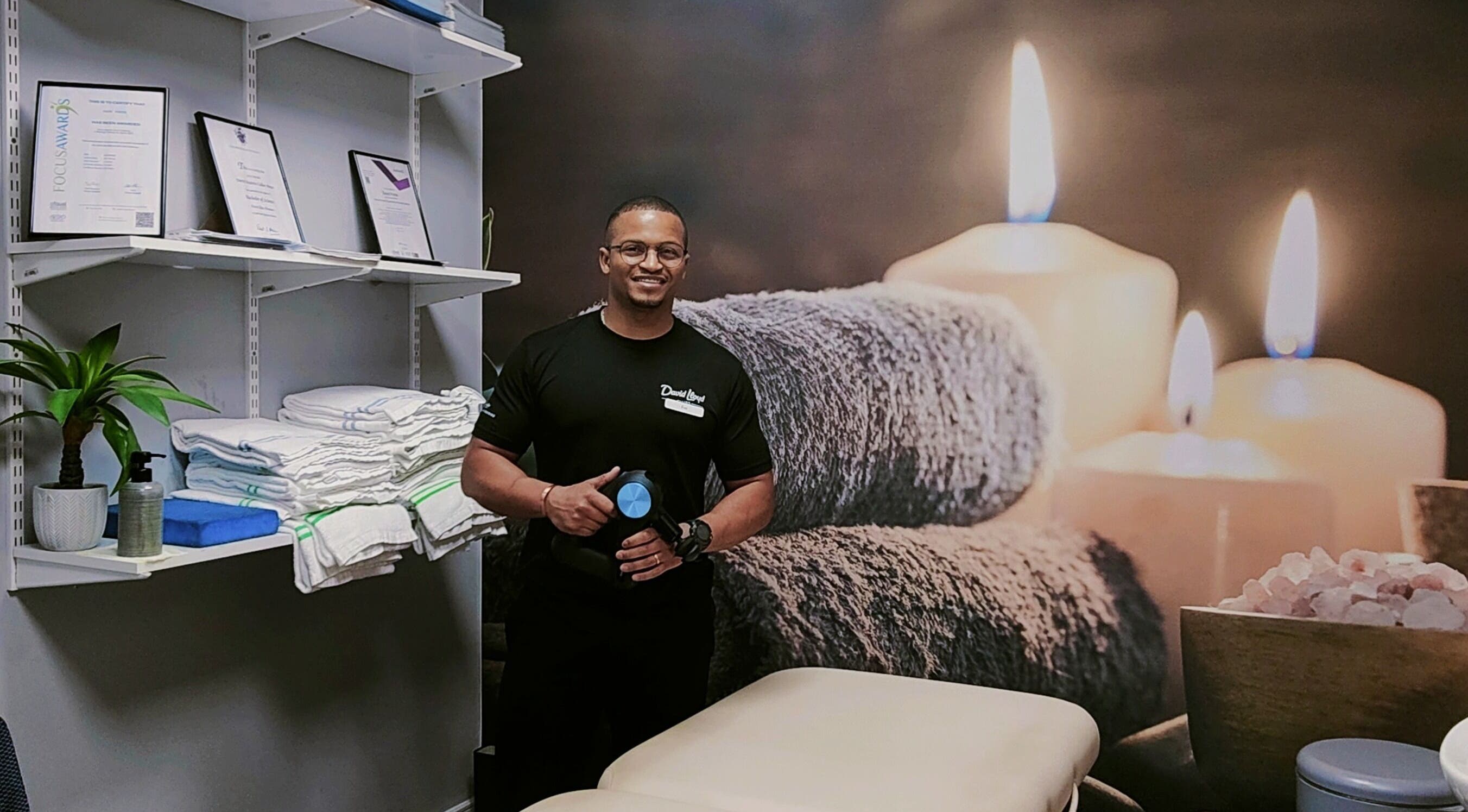 Massage therapist at VVV, Nottingham, GB, with calming candles and towels in a serene treatment room.