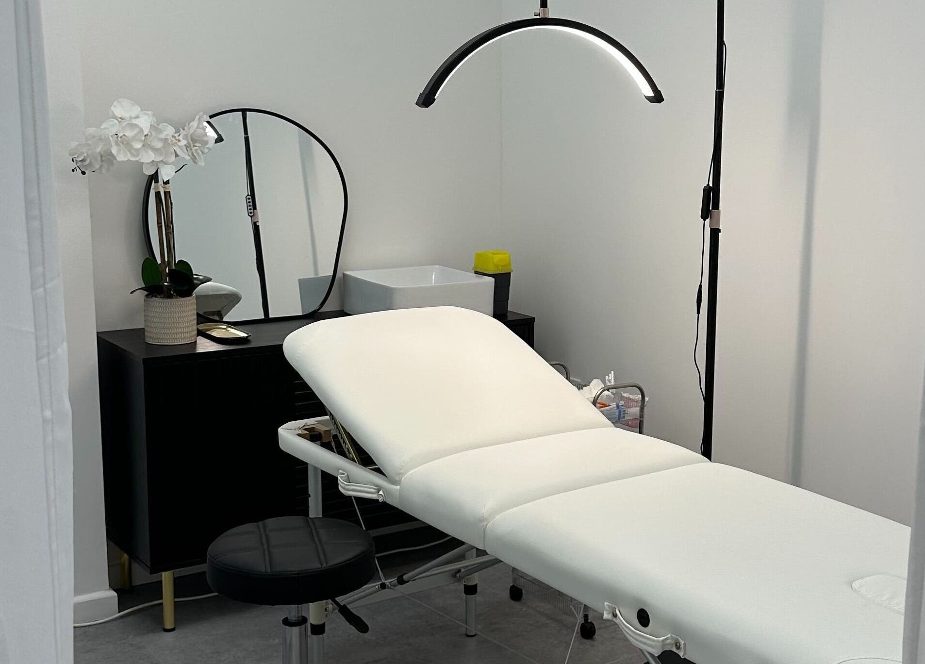 PM Aesthetics in Cardiff, Wales, GB showcases a serene treatment room with a white bed and floral decor.