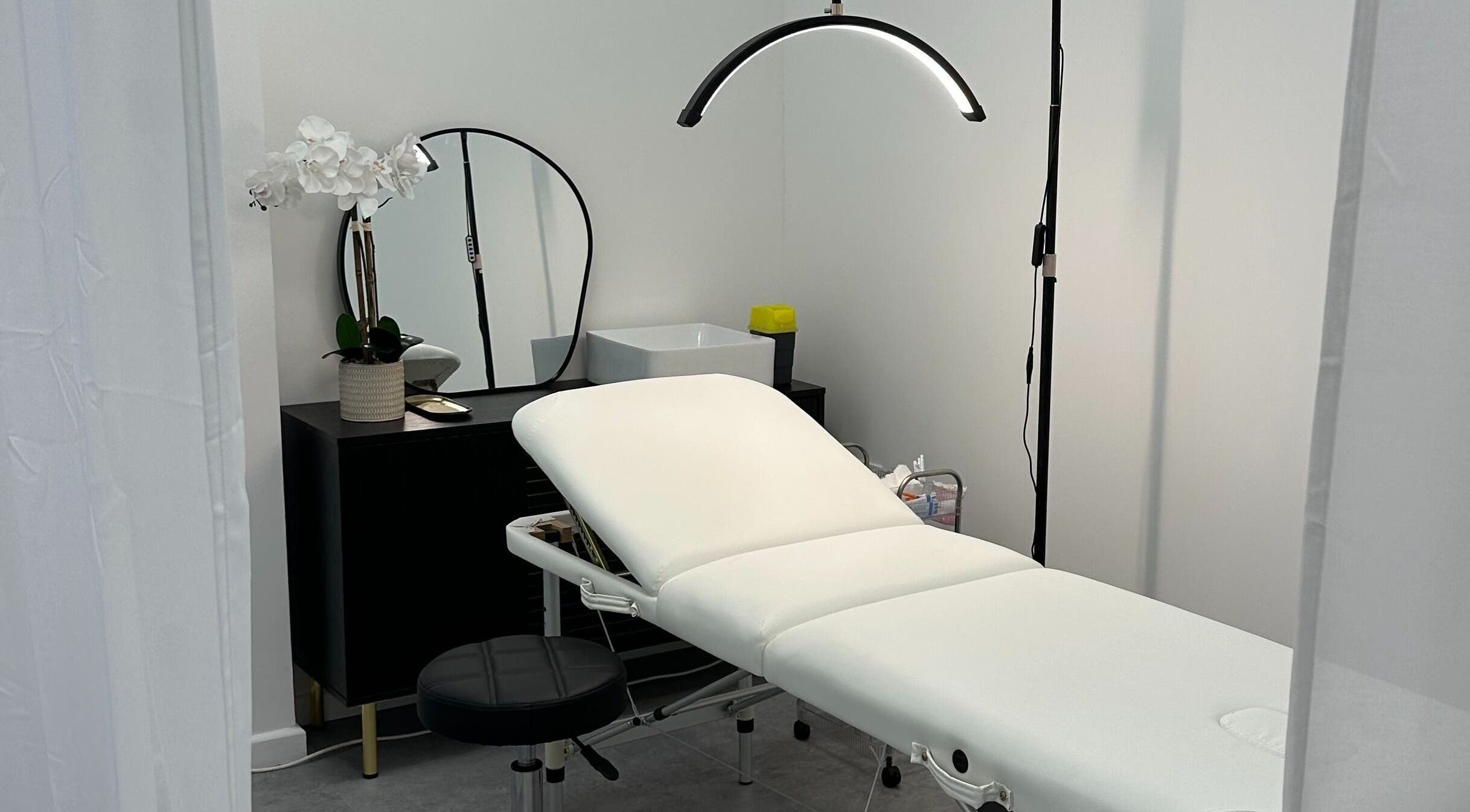 PM Aesthetics in Cardiff, Wales, GB showcases a serene treatment room with a white bed and floral decor.