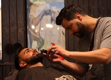 Barber at Carlsens Barbershop in Svendborg, DK grooming a client's beard with precision tools.