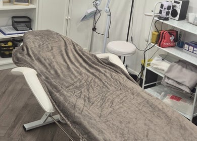 Cozy treatment room at YM London, London, England, GB, featuring a comfortable therapy bed and organized shelves.