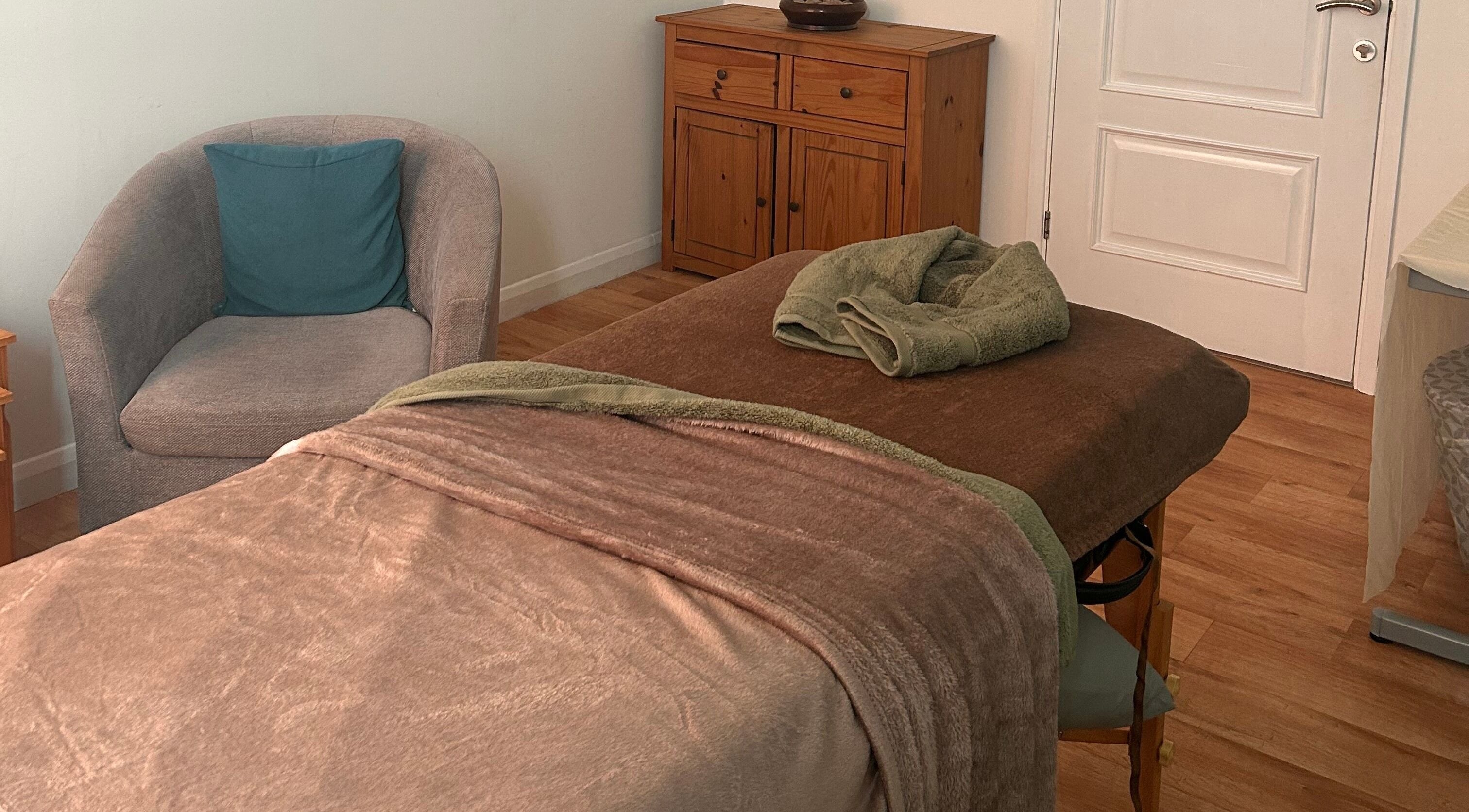 Relaxing massage room at Thyme to Unwind Therapies in Gloucester, England, GB with cozy chair and table.