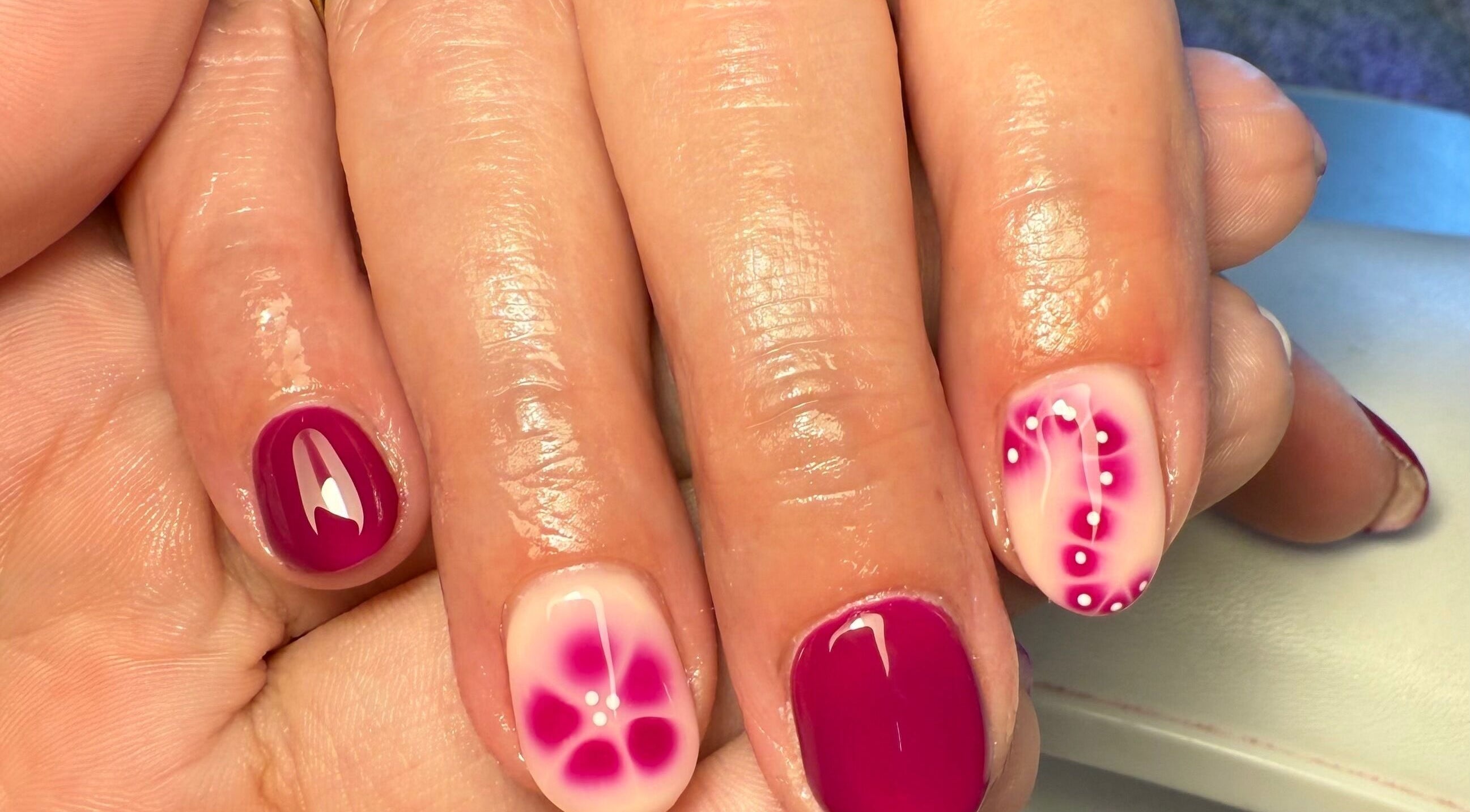 Elegant floral nail art at Daisie Mae Beauty, Lechlade, England, GB. Vibrant pink and white manicure design.