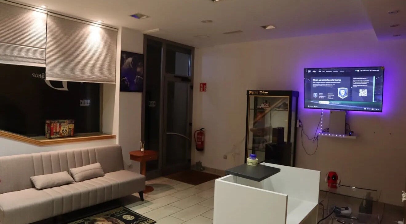 Interior moderno de Vramens Barber Shop en Agurain, Euskadi, ES con sofá gris y televisor.