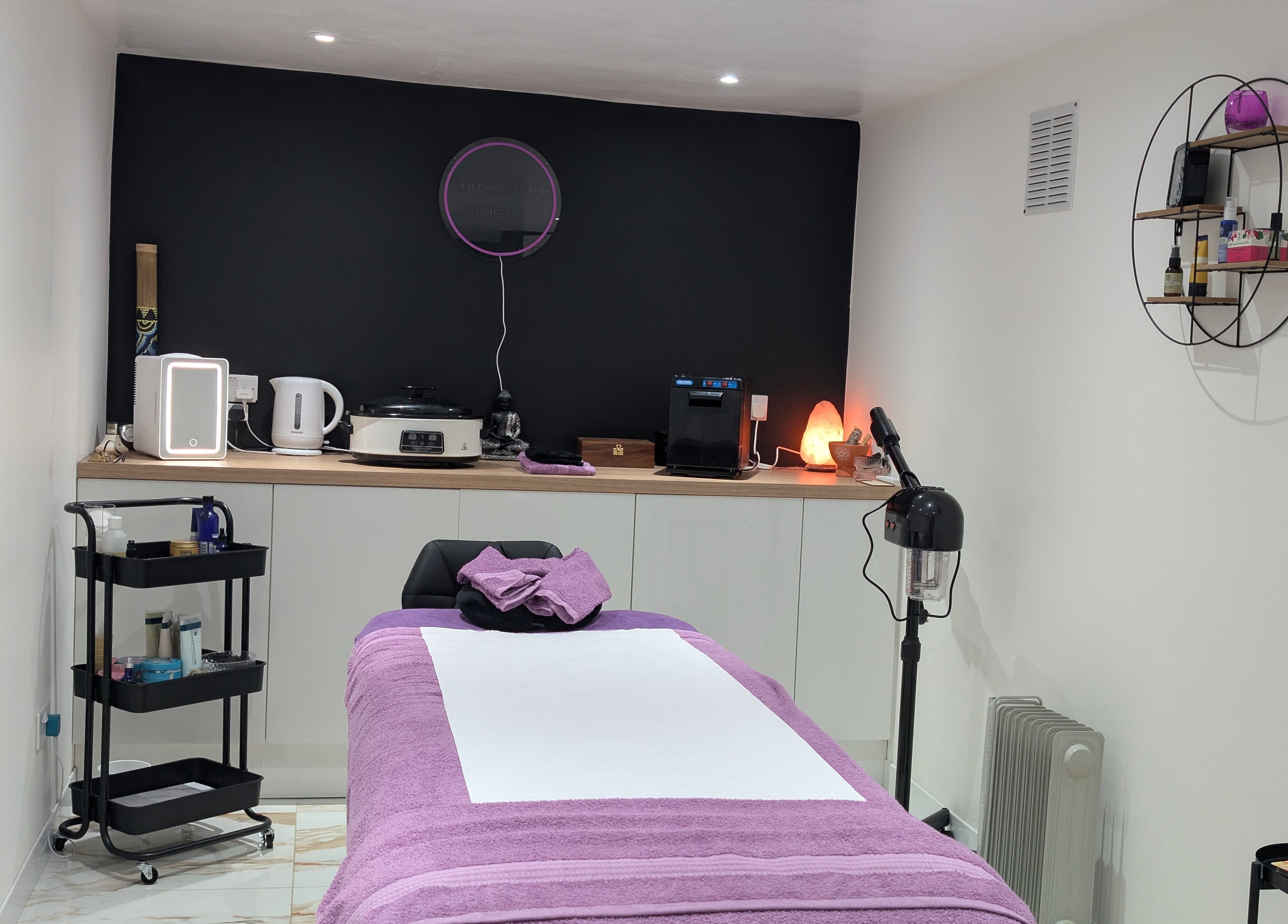Cozy treatment room at Purple Crown Holistics, Eston, England, with a purple massage table and shelves.