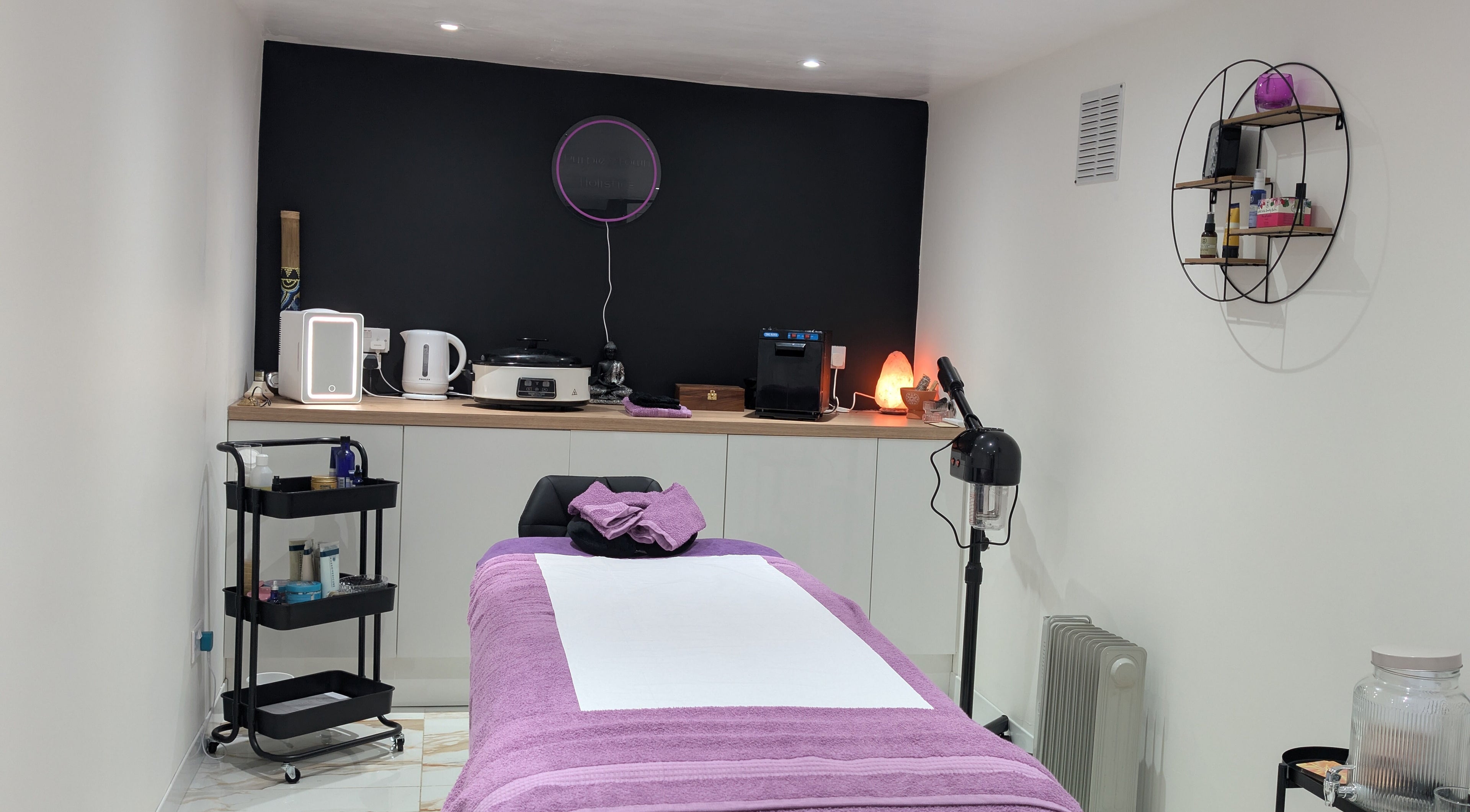 Cozy treatment room at Purple Crown Holistics, Eston, England, with a purple massage table and shelves.
