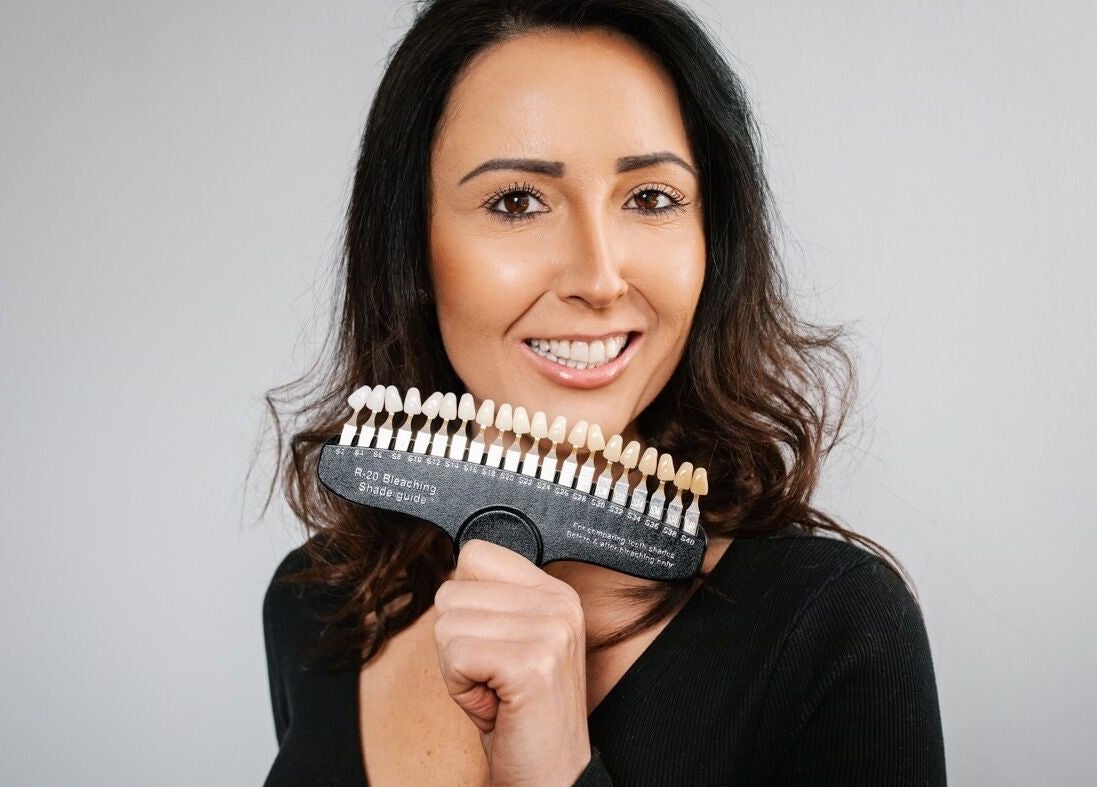 Woman showcasing teeth shade guide at B-Radiant, Briton Ferry, Wales, GB, highlighting professional whitening services.