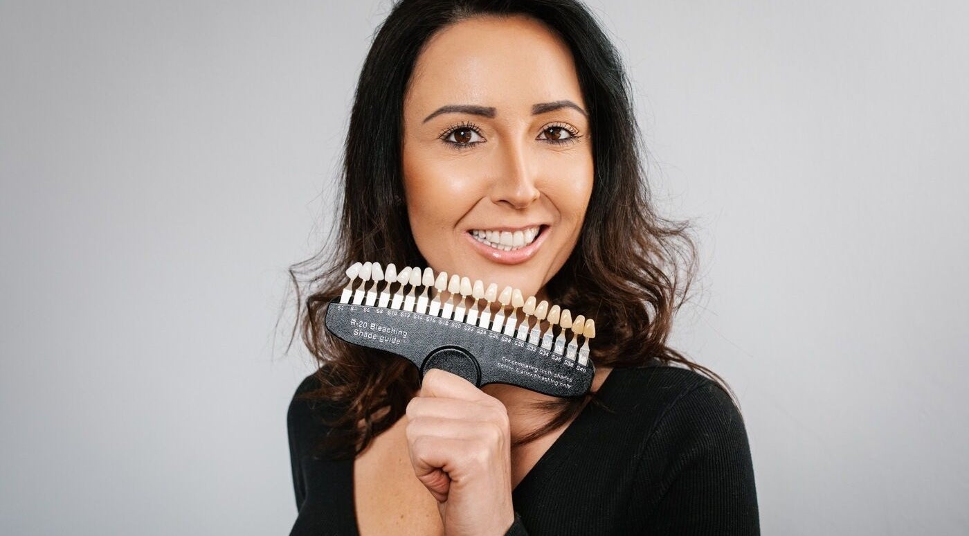 Woman showcasing teeth shade guide at B-Radiant, Briton Ferry, Wales, GB, highlighting professional whitening services.