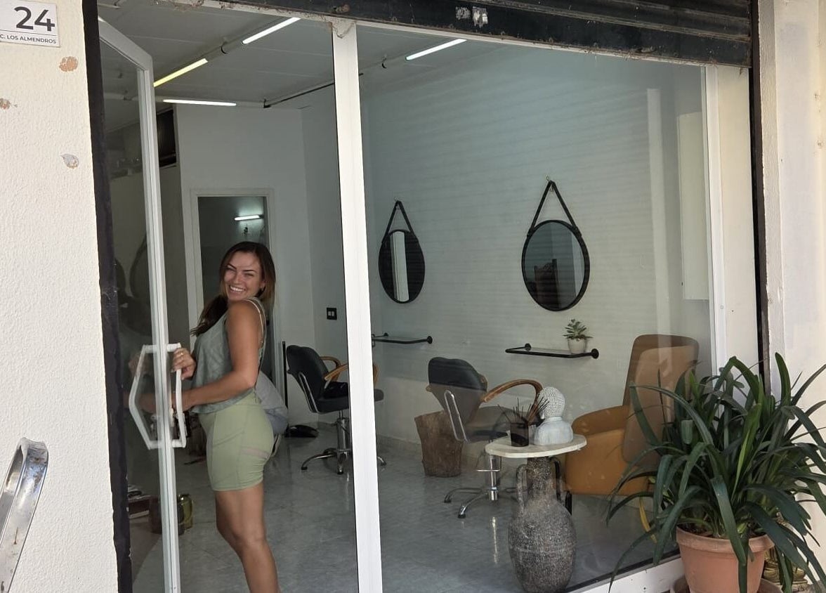 Smiling woman entering Hair by joshua james salon, Mallorca, Illes Balears, ES, with stylish interior visible.