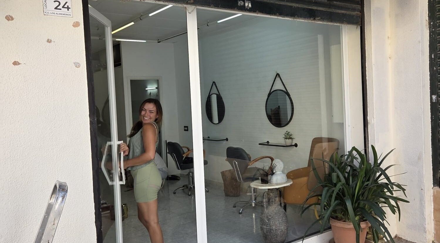 Smiling woman entering Hair by joshua james salon, Mallorca, Illes Balears, ES, with stylish interior visible.
