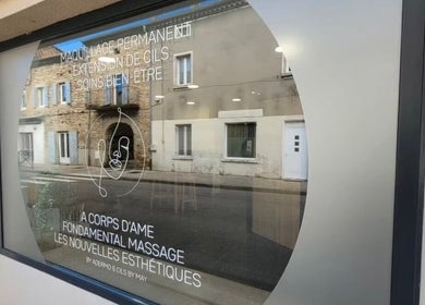 Vitrine de Fondamental Massage à Saint-Privat, Auvergne-rhône-alpes, FR, reflétant un bâtiment en face.