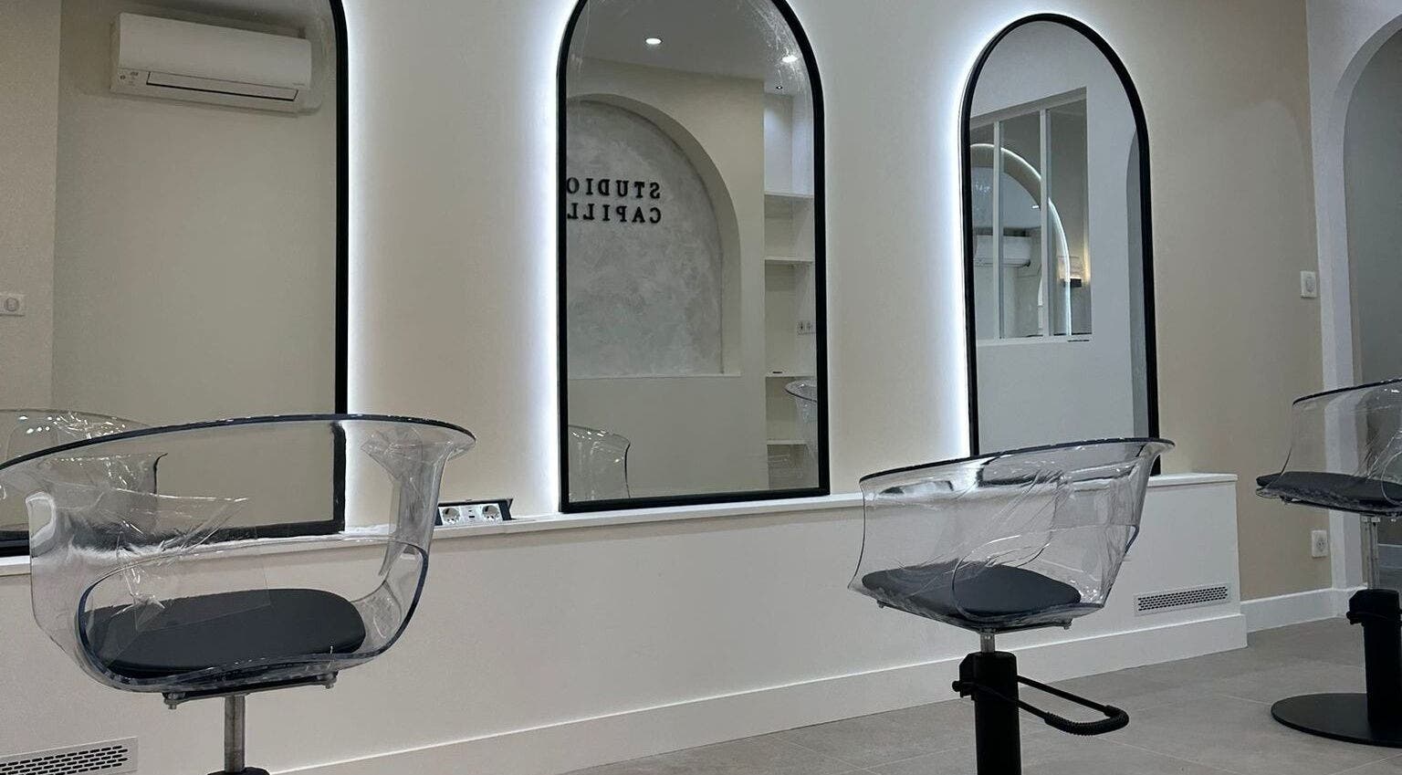 Salon moderne STUDIO CAPILLAIRE à Suresnes, Île-de-France, avec sièges transparents et grands miroirs.