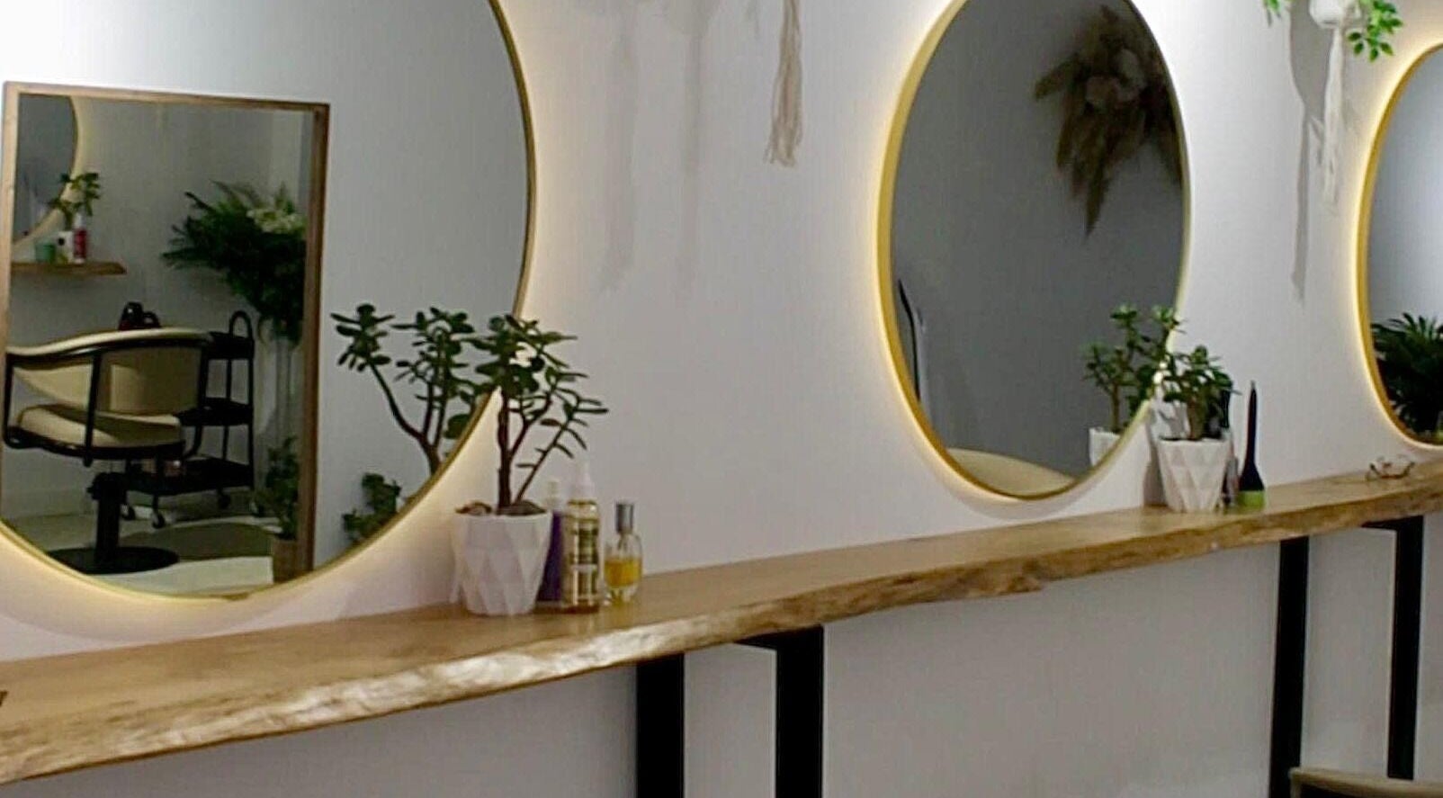 Interior elegante do Kairós Beauty Lounge em Pedrouços, Porto, PT, com espelho redondo iluminado e plantas.