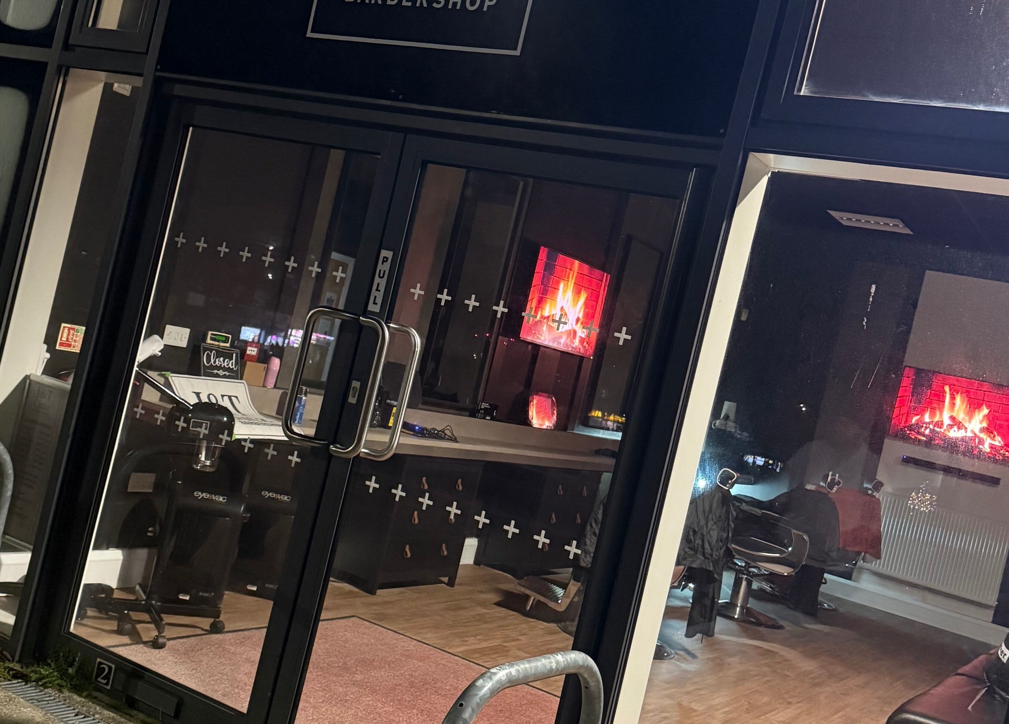 J&T Cutz LTD in Bristol, England. Warm interior with lit fireplace seen through glass doors.