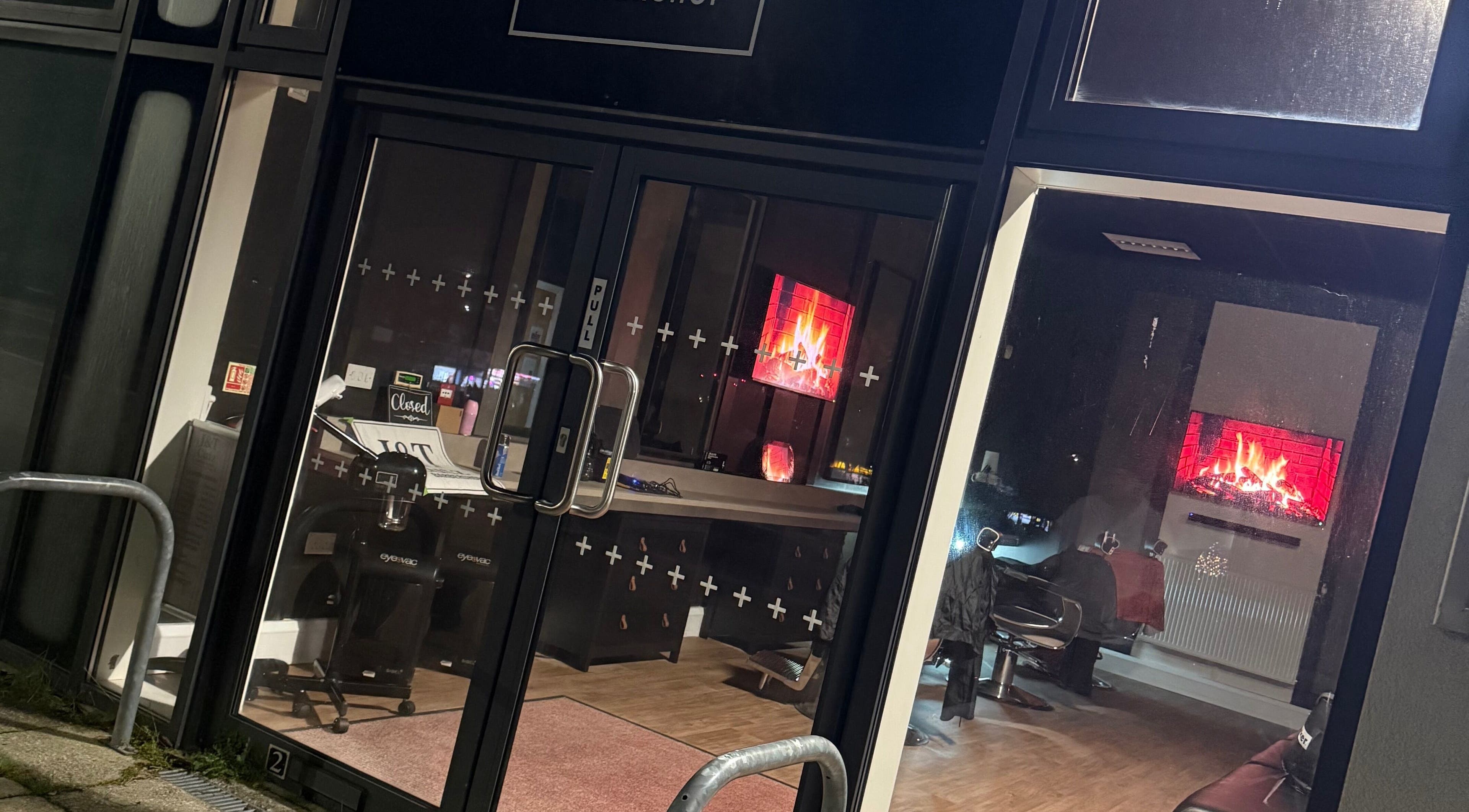 J&T Cutz LTD in Bristol, England. Warm interior with lit fireplace seen through glass doors.